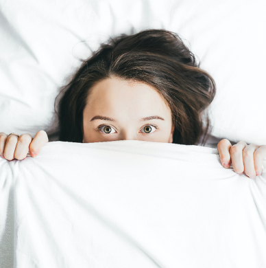 Mulher jovem deitada na cama e parcialmente coberta pelos cobertores